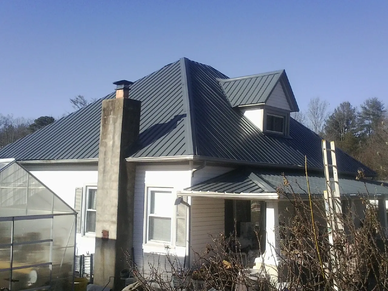 Dark blue standing seam metal roof on a white farmhouse with dormer — Slate & Tile Roof Repair by Roofing Brothers in Holton