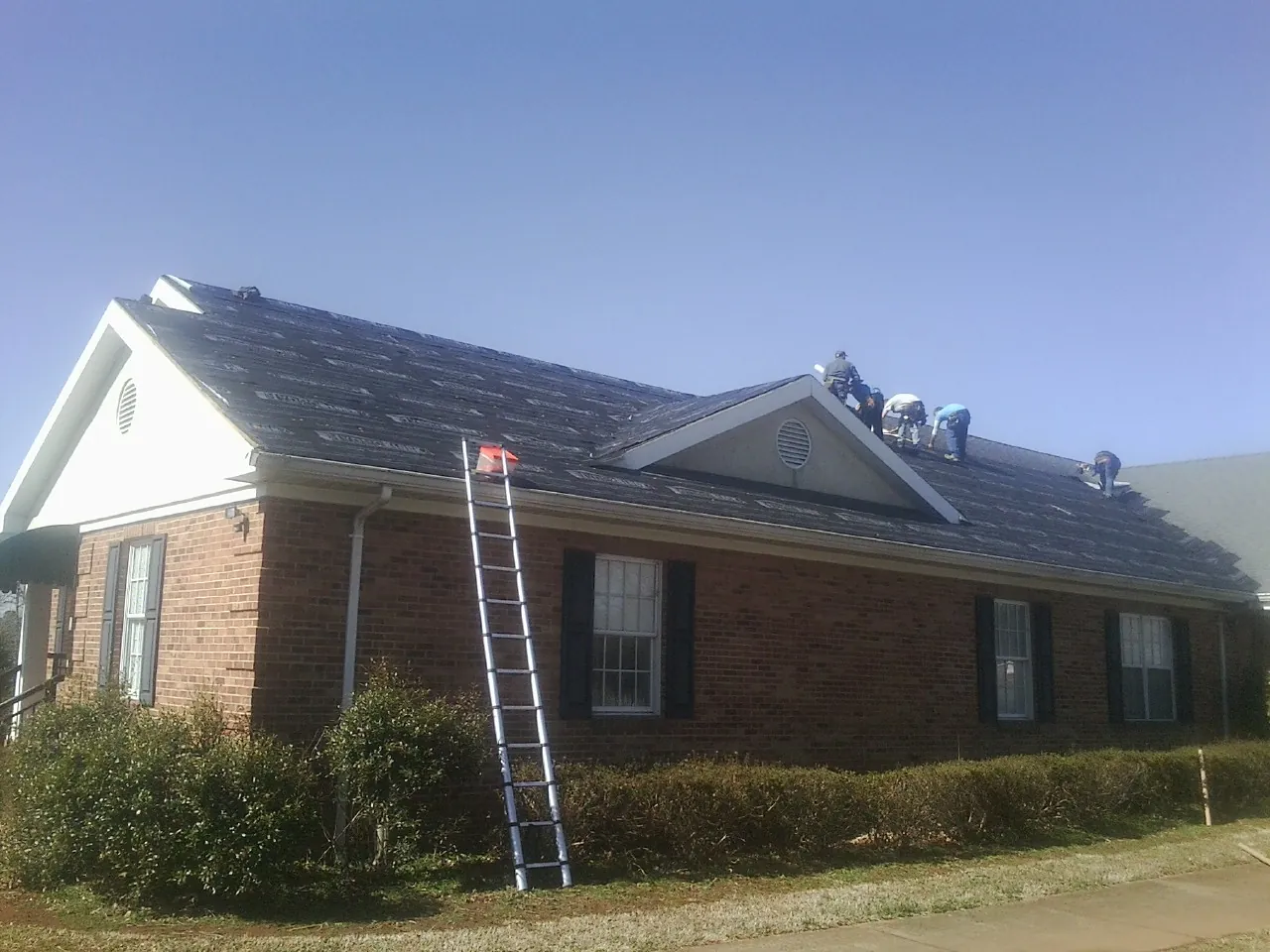 Crew tearing shingles off a brick ranch roof with a ladder set — Emergency Roof Repair work by our crew in Holton