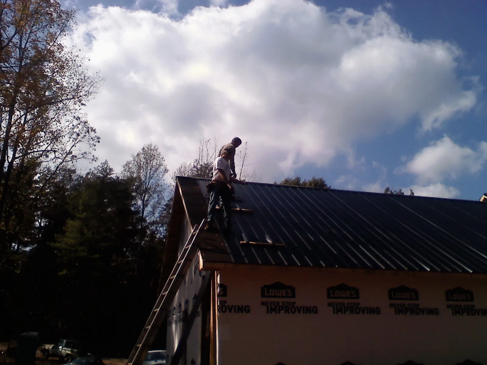 Roofer fastening dark metal panels high against a cloudy sky, from a Roof Inspection job in Holton